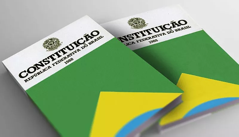 Uma foto de dois grandes livros com parte da bandeira do Brasil na capa, escrito "Constituição - Republica Federativa do Brasil 1988"